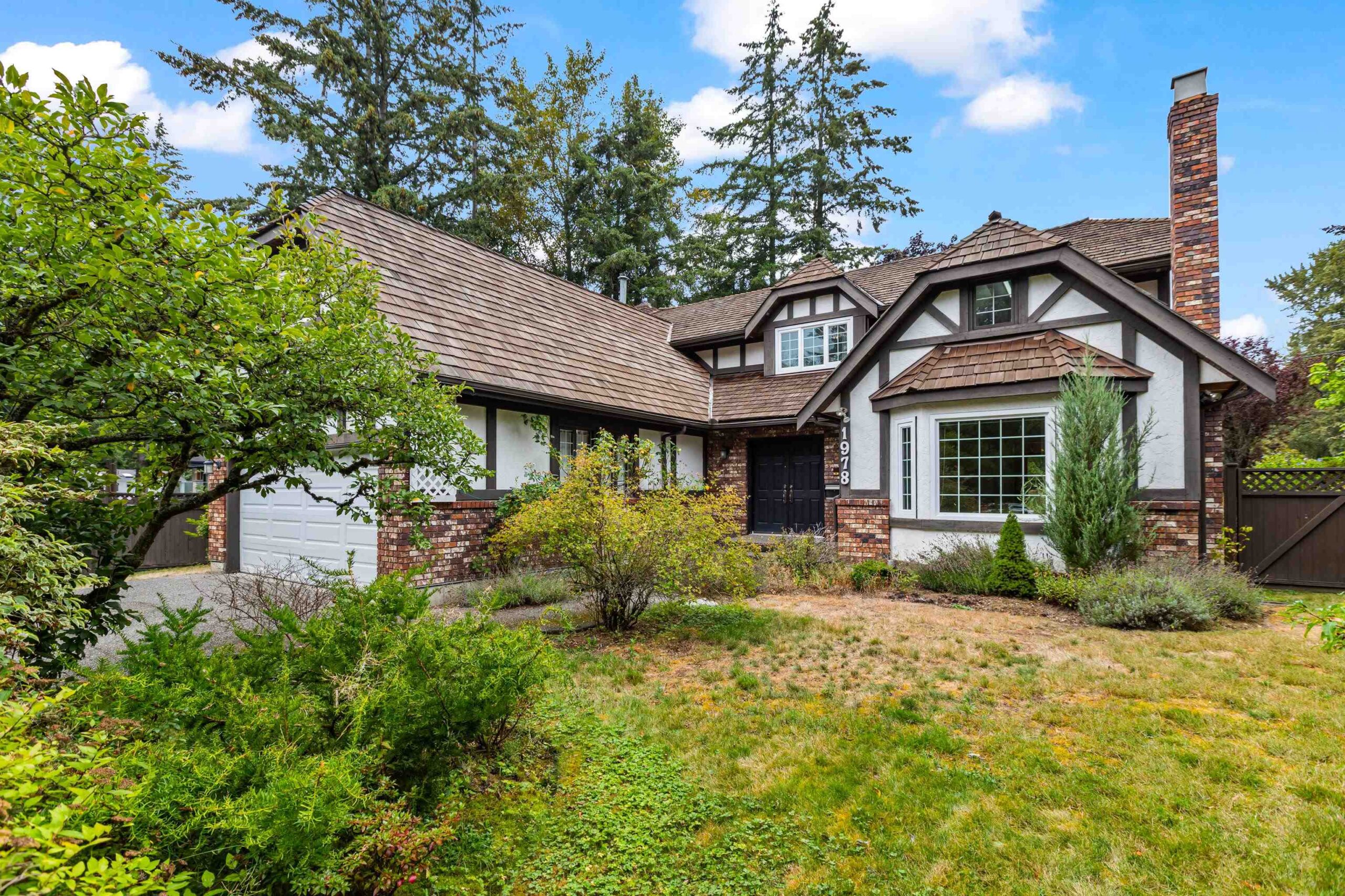 Charming Tudor-style home with brick and timber detailing, nestled among lush greenery in Amblegreene. This front elevation showcases the character and curb appeal of a recent purchase facilitated by South Rock Real Estate Group.