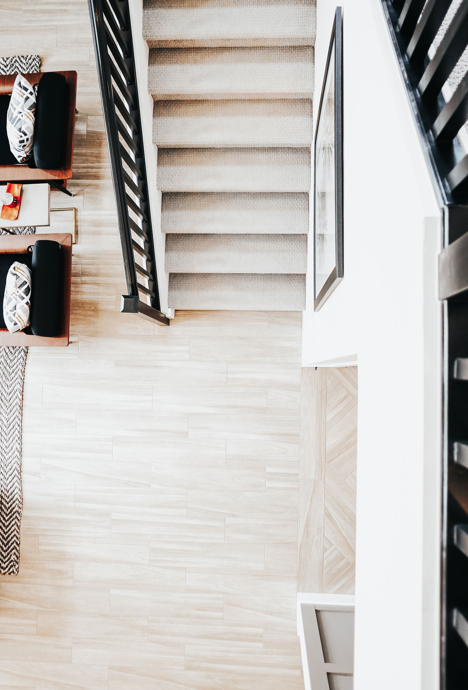 Modern home interior with a carpeted staircase, black railings, and a bright open-concept living space featuring wood-look flooring, neutral tones, and contemporary furniture.